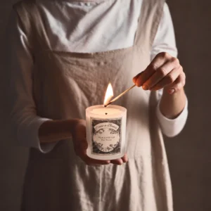 Pear & Vetiver Signature Candle by Clare a Beau’s being lit by hand in a softly styled neutral setting.