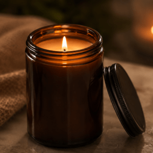 Luxury amber glass scented candle with black lid, lit in a warm cosy setting